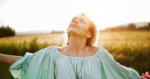 Free-spirited woman in a flowing mint-green dress, arms outstretched, enjoying the warmth of the sun in an open field.