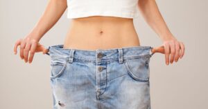 Close-up of a person pulling out the waistband of oversized jeans, symbolizing weight loss success.