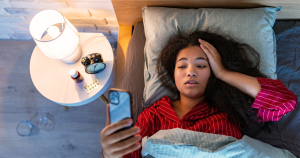 A young woman struggling with insomnia while scrolling her phone in bed — a common late-night routine linked to sleep issues and stress.