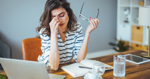 A stressed woman sitting at her desk holding her head, showing signs of burnout and anxiety while working on her laptop.