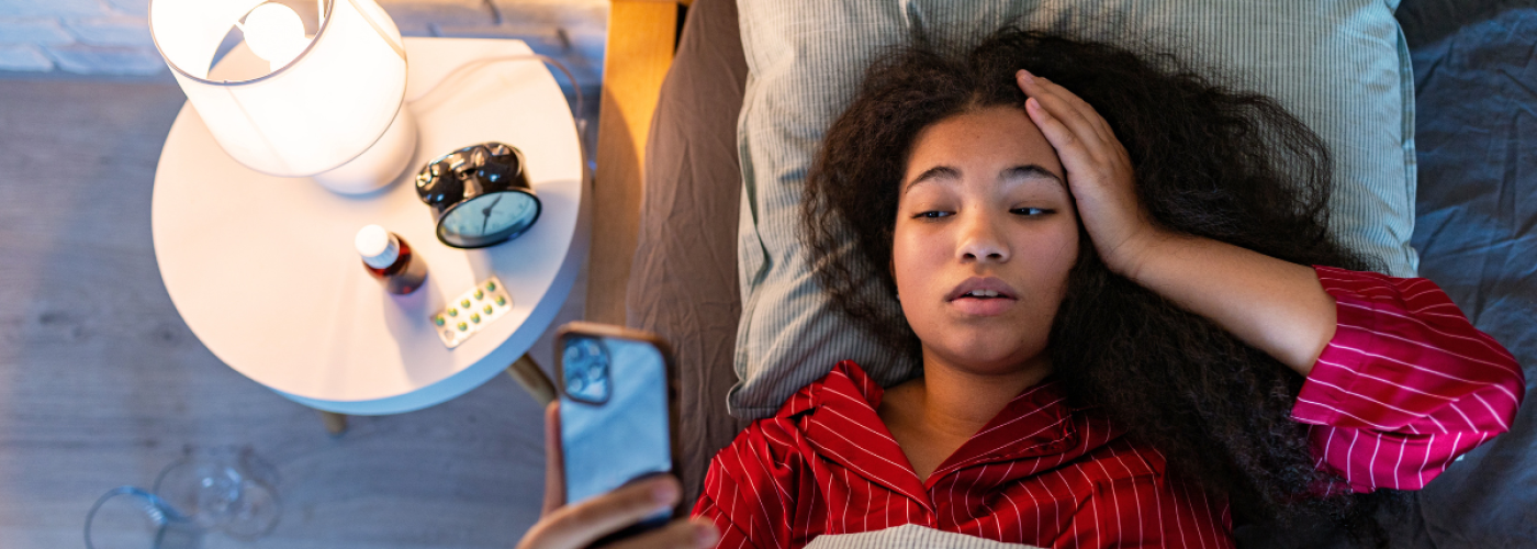 A young woman struggling with insomnia while scrolling her phone in bed — a common late-night routine linked to sleep issues and stress.